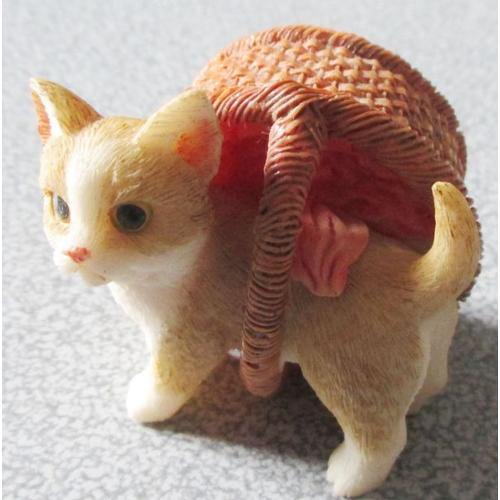 Figurine faite d'un petit chat blanc et beige collé sur un panier d'osier coloré qu'il semble porter sur son dos-5x6x4cm environ- tient debout sur les pattes du chat ou posé sur le panier
