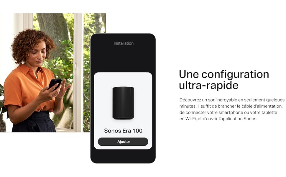 une femme debout devant une fen�tre tenant un smartphone.